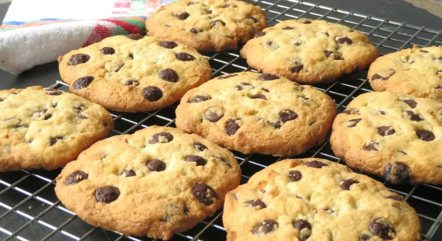 Un montón de galletas con pepitas de chocolate recién horneadas, doradas y deliciosas, enfriándose en una rejilla.