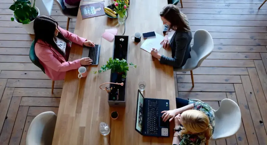 Kobiety pracują przy drewnianym stole. Jedna pisze na laptopie, druga notuje. To przykład, jak etyka co to, wpływa na codzienne zadania.