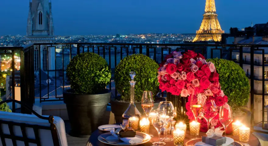 Cena romántica en París para San Valentín. Mesa con rosas, velas y Torre Eiffel iluminada al fondo.