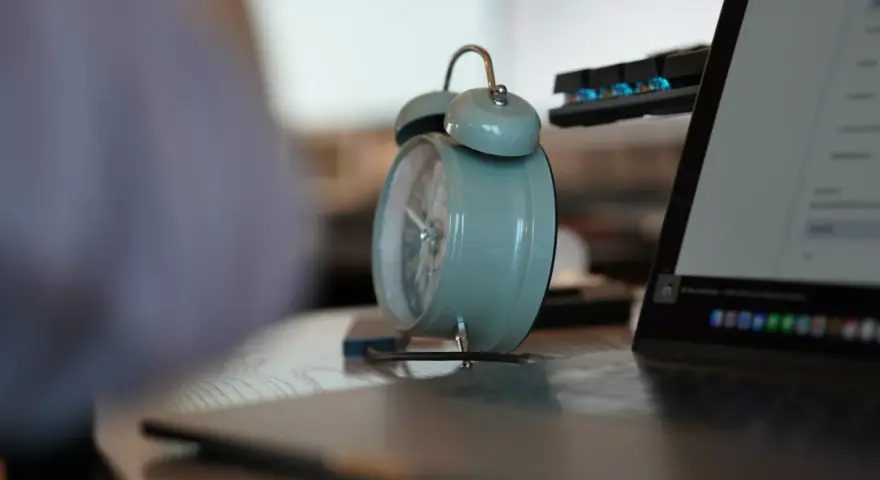 Budzik obok laptopa przypomina o pracy. 3/4 etatu ile to godzin? Czas na efektywność!