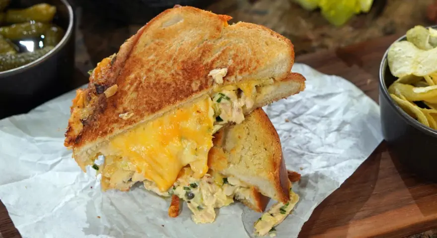 Ein köstlicher Tuna Melt mit geschmolzenem Käse, serviert mit Gurken und Chips.