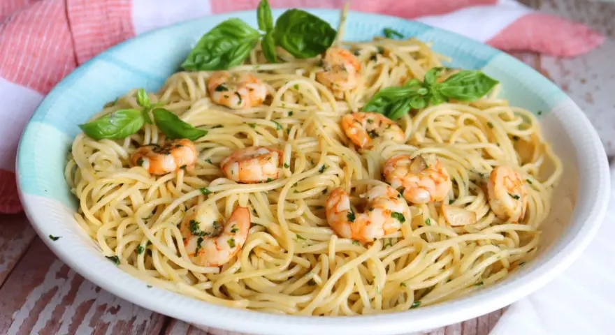 Un plato de espaguetis con gambas, adornado con hojas de albahaca fresca y perejil picado.