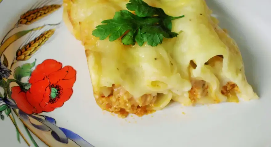 Cannelloni z mięsem i beszamelem przepis. Pyszne danie zapieczone pod beszamelem, udekorowane natką pietruszki, na talerzu z makami.