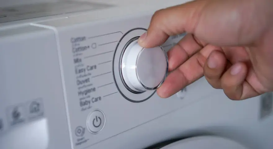 Mano ajustando el selector de la lavadora para saber como lavar un anorak. Se ven programas como "Cotton", "Mix", "Duvet".