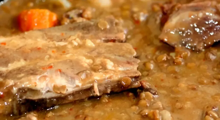 Guiso de lentejas con costillas, zanahoria y trozos de carne en un caldo espeso.