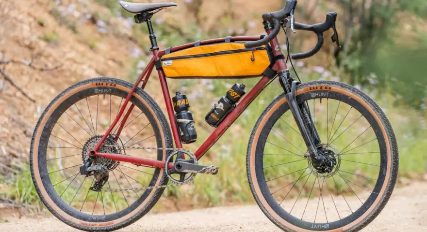 A red gravel bike with an orange frame bag and two water bottles. This bike, like many gravel bikes, does not have suspension, relying on its tires and frame for comfort.