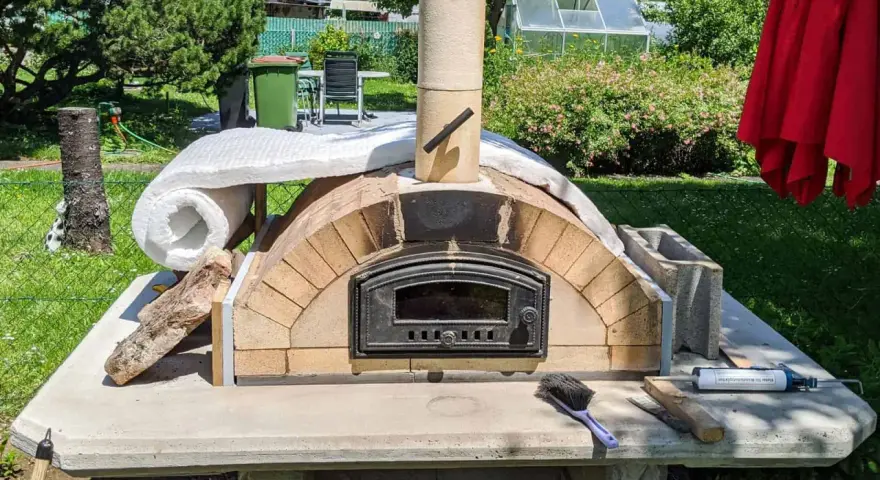 Ein selbstgebauter Pizzaofen im Garten, noch in der Bauphase, mit Isolierung und Schornstein. Bald bereit für die erste Pizza!