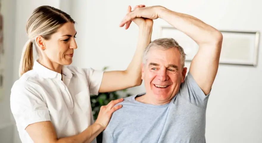 Physiotherapeutin unterstützt Mann bei Übungen zur Wiederherstellung der Beweglichkeit nach Schlaganfall. Verordnung Physiotherapie nach Schlaganfall wird umgesetzt.