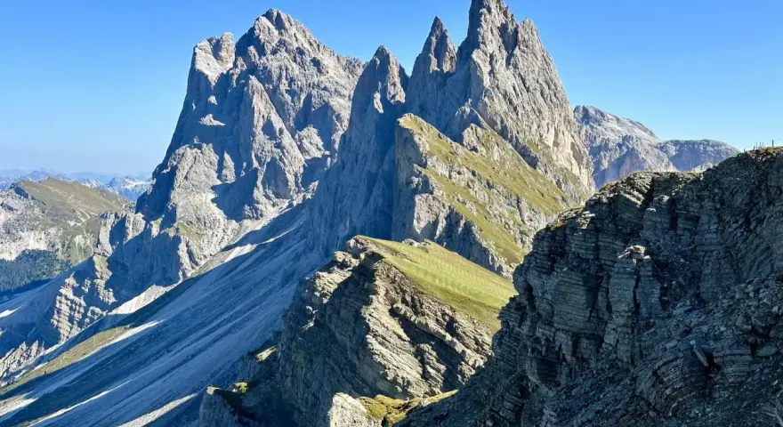 Majestätische Felszinnen ragen in den blauen Himmel. Eine **Seceda Wanderung** führt durch grüne Almwiesen und felsiges Gelände.