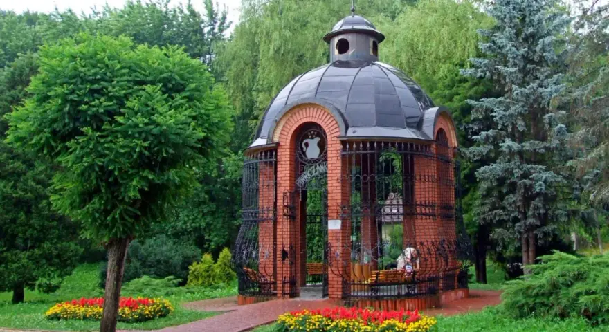 Urokliwa pijalnia piwniczna z cegły z czarną kopułą, otoczona zielenią i kolorowymi kwiatami.