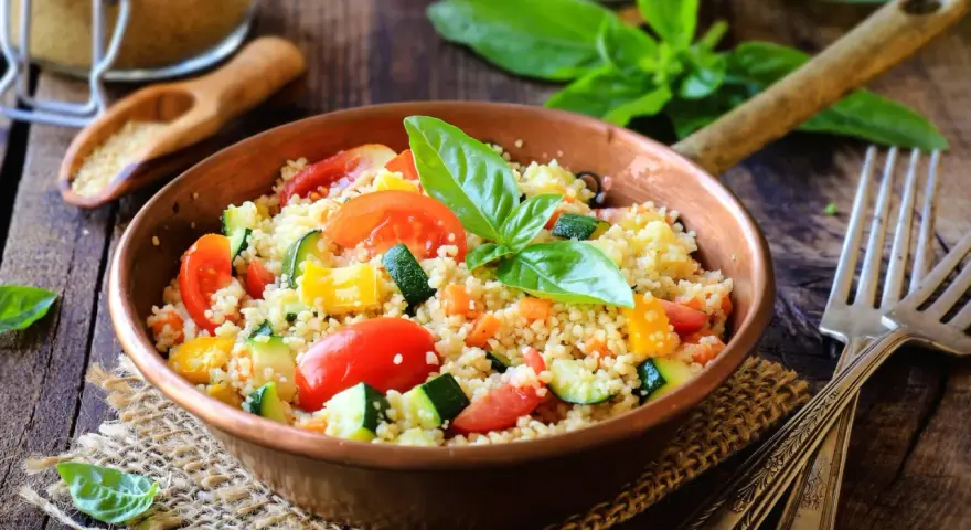 Un piatto colorato con couscous, pomodori, zucchine e peperoni, perfetto per una ricetta cous cous originale e fresca.
