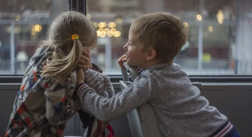 Bambina con disturbo della comunicazione sociale si nasconde, mentre un bambino le parla con un sorriso.