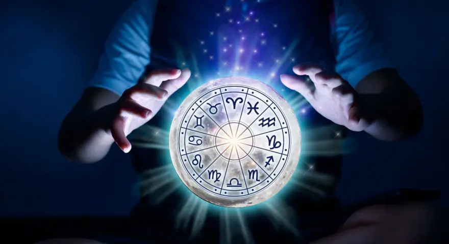 Dłonie unoszą księżyc z tarczą zodiaku, gdzie znaki zodiaku i żywioły splatają się w mistycznym świetle.