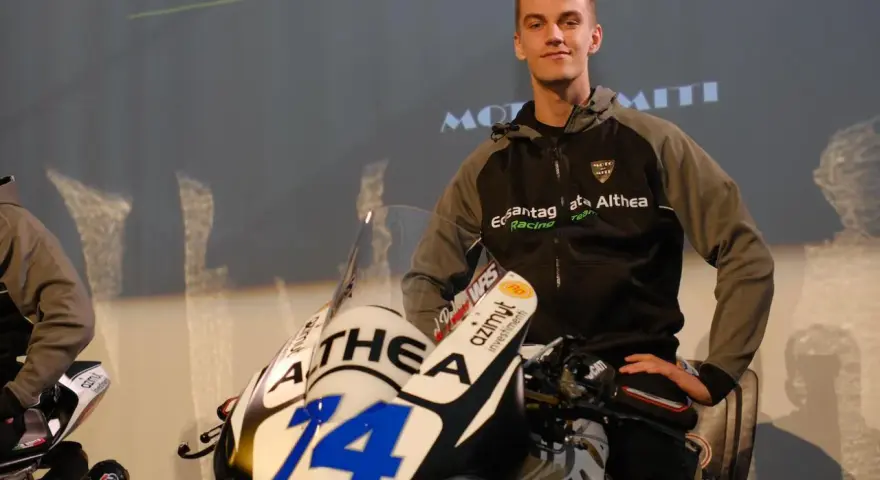 Piotr Biesiekirski, młody kierowca wyścigowy, pozuje obok swojego motocykla z numerem 14.