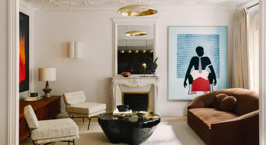 Un dormitorio eclectico con sofá marrón, dos sillones de tweed, mesa de centro de piedra negra, chimenea de mármol y arte abstracto vibrante.