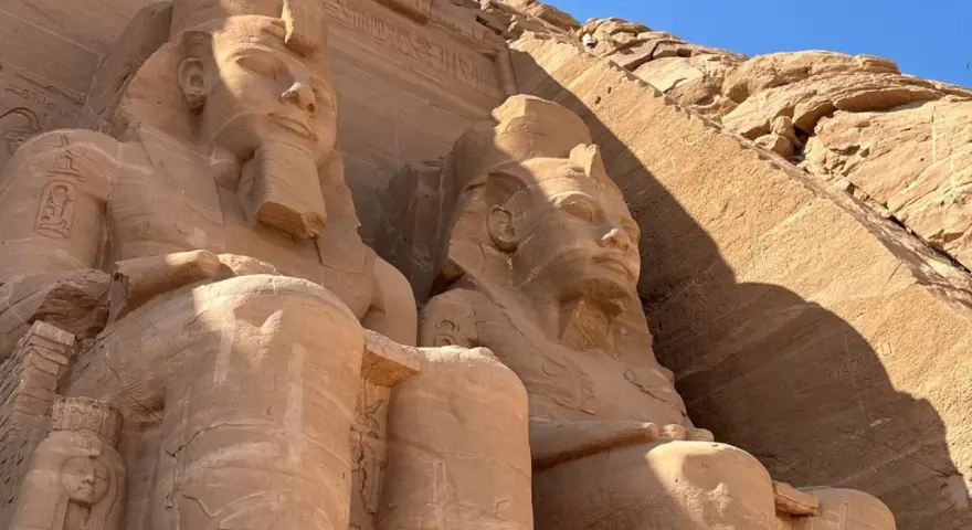 Gigantyczne kamienne posągi faraonów w Abu Simbel, Egipt, na tle skalnej ściany i błękitnego nieba.