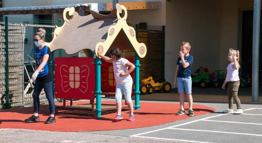 Une animatrice, masque et gants, surveille des enfants sur un terrain de jeu. Le directeur ACM veille à la sécurité.