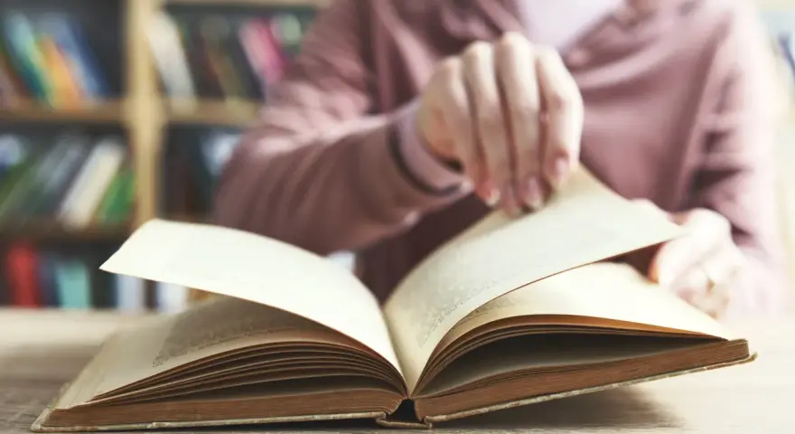 Otwarta księga na stole, w tle regały pełne książek. To początek podróży przez arcydzieła literatury światowej, lista skarbów do odkrycia.