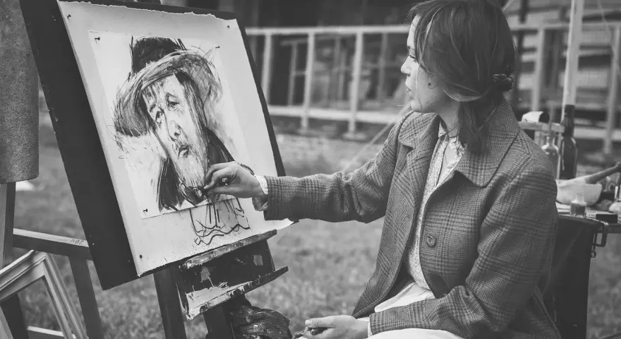 Artystka tworzy portret węglem. Jej ręka z pędzlem zbliża się do płótna, gdzie widoczna jest plama rysunek.
