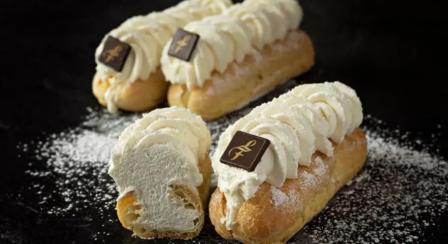 Trois éclairs chantilly généreusement garnis de crème fouettée, ornés d'un carré de chocolat, saupoudrés de sucre glace.