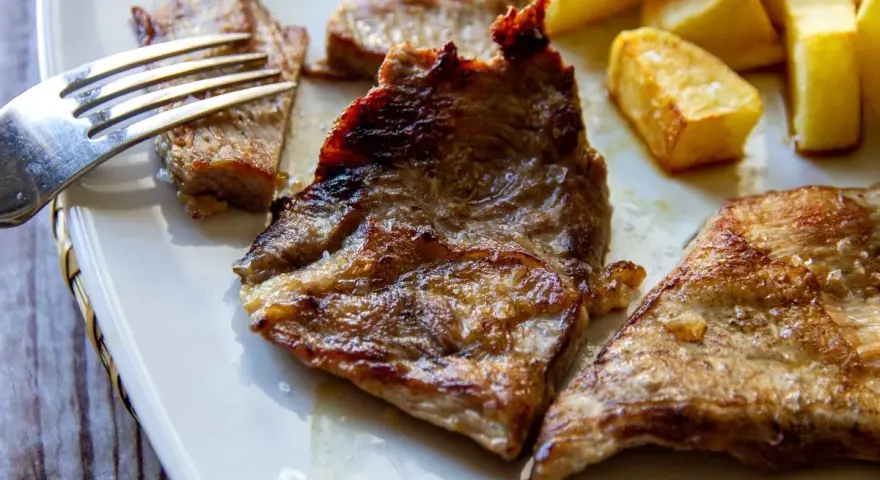 Jugosa blanqueta de cerdo a la plancha, servida con patatas fritas doradas. Un plato perfecto para disfrutar.