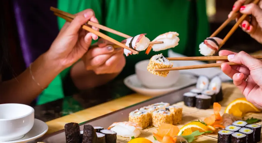 Ręce trzymają pałeczki, jedząc sushi. To smakowita uczta, która odzwierciedla japońskie tradycje kulinarne.