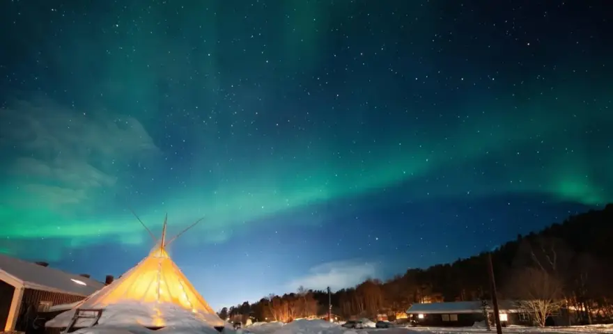 Nocne niebo nad nordkapp camping rozświetla zorza polarna. W dole ośnieżony teren i oświetlony namiot.