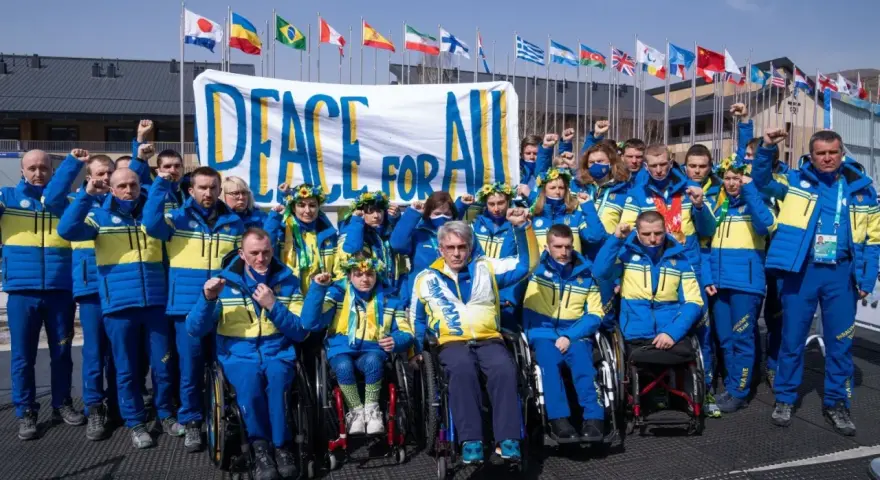 Ukraińska drużyna paraolimpijska z podniesionymi pięściami przed transparentem "Peace for All". Nadzieja na pokój na igrzyskach paraolimpijskich 2026.