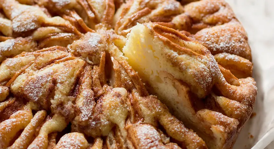 Una deliziosa torta di mele, cosparsa di zucchero a velo, con una fetta appena tolta che rivela la morbidezza dell'impasto e le mele caramellate.