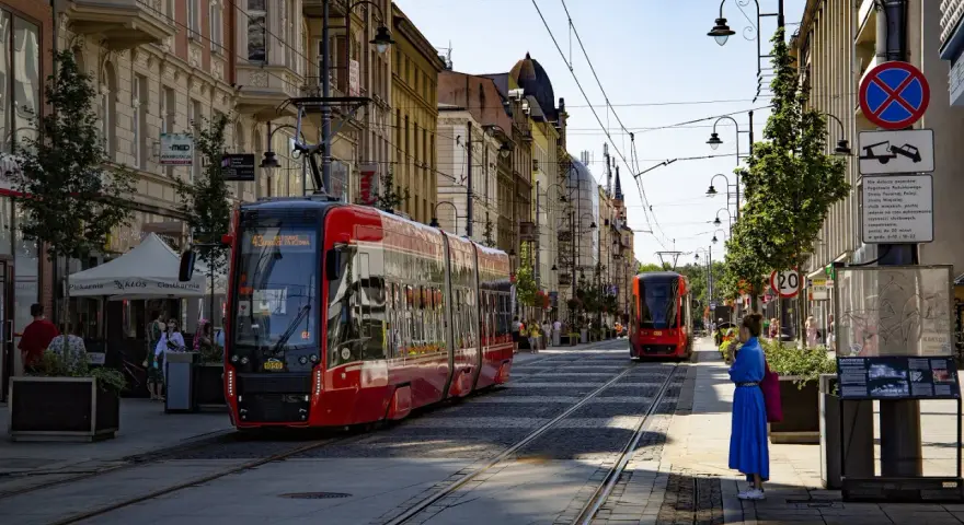 Czerwony tramwaj na ulicy w Katowicach. W tle kamienice i inny tramwaj. To widok na katowice stare miasto.