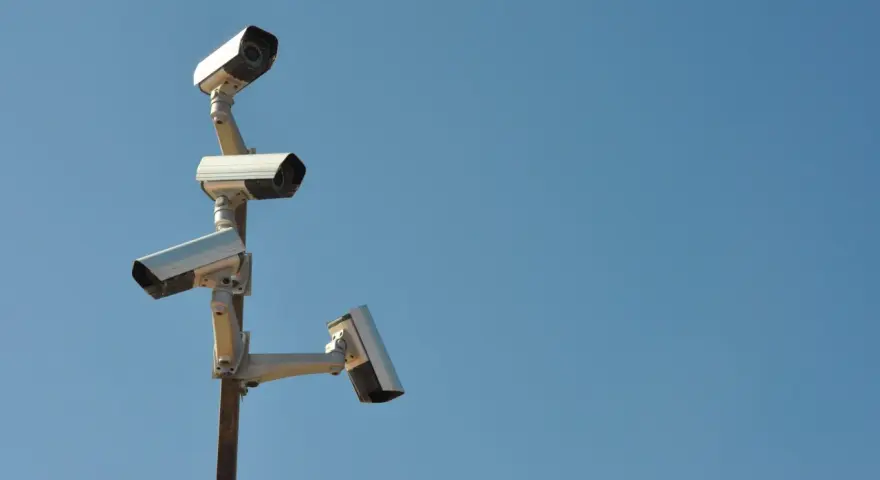 Cztery kamery monitoringu na słupie, czujne oko inwigilacji wpatrujące się w błękitne niebo.
