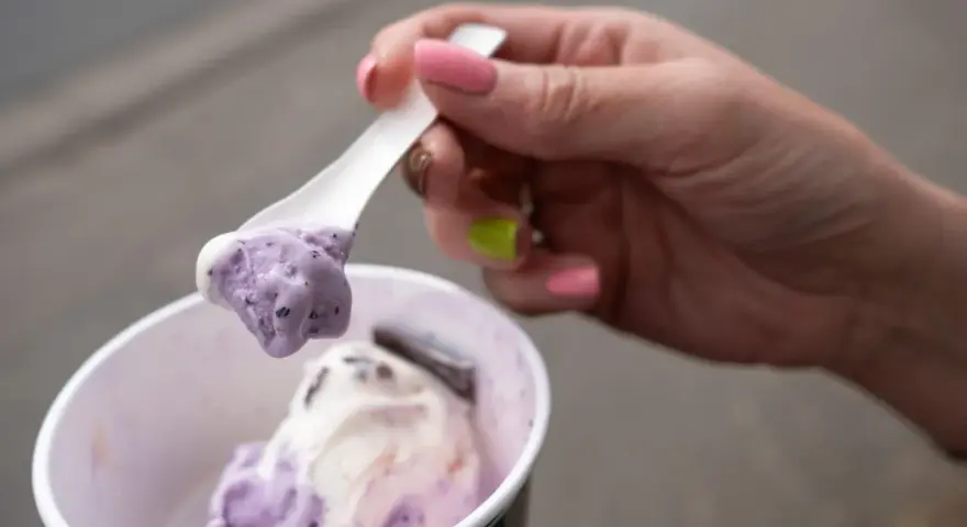 Eine Hand mit pink lackierten Nägeln hält einen Löffel mit zwei Kugeln Eis im Becher, italienisch.