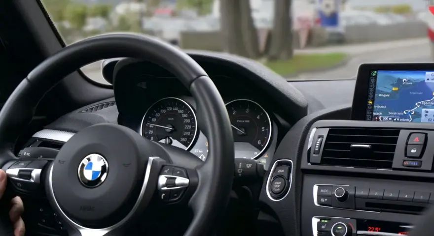 Wnętrze BMW z kierownicą i nawigacją. Kierowca sprawdza plan serwisowy przed podróżą.