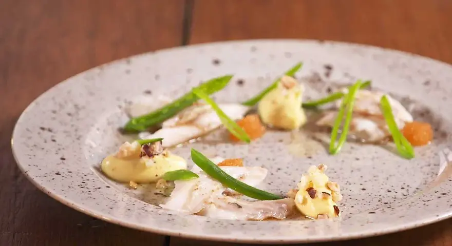 Vacker tallrik med piggvar recept: vit fisk, gröna bönor, orange rom och en krämig sås med nötter.