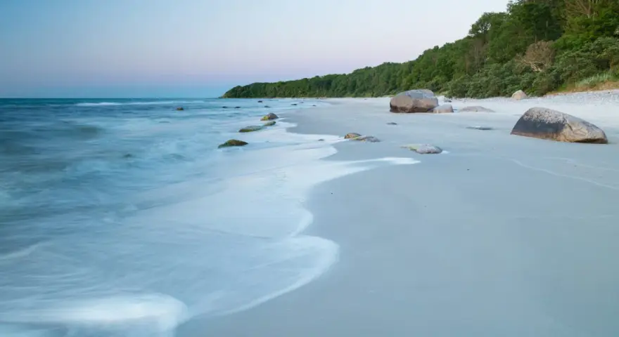 Spokojne plaże nad Bałtykiem o świcie, z delikatnymi falami i kamieniami na piasku.