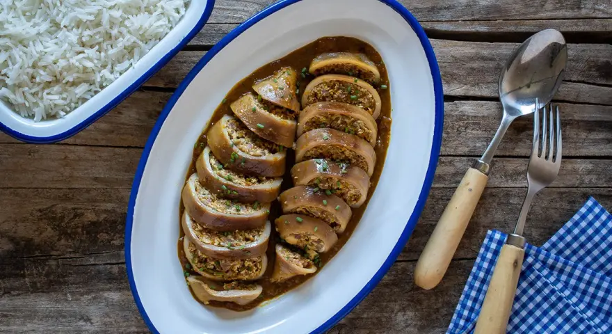 Calamares rellenos en salsa, servidos en una bandeja ovalada junto a un bol de arroz blanco. Cubiertos con cebollino picado.