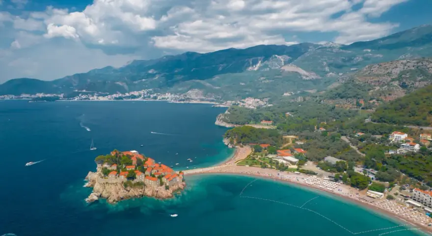 Sveti Stefan, Czarnogóra czy warto? Widok z lotu ptaka na malowniczą wyspę połączoną z lądem, turkusowe morze i górzyste wybrzeże.