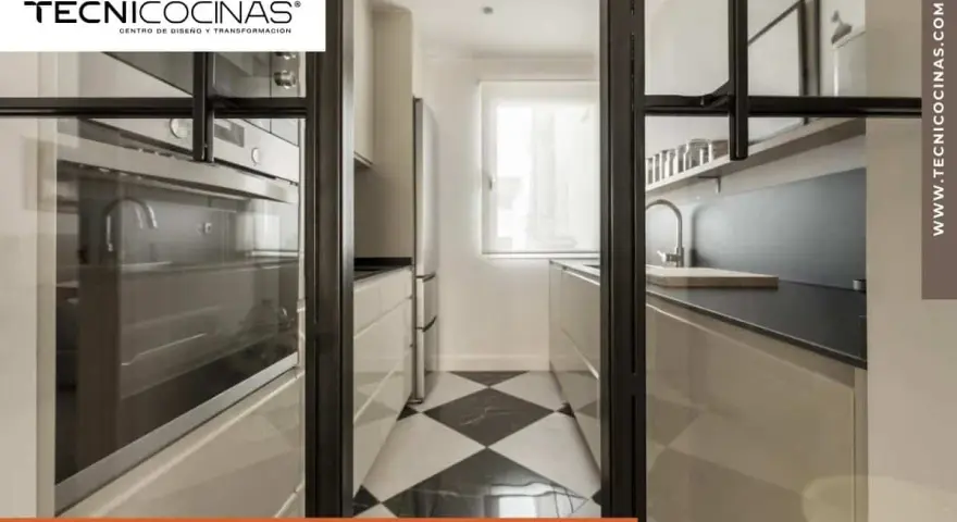 Cocina semiabierta cristal con suelo de damero, electrodomésticos integrados y encimera moderna.