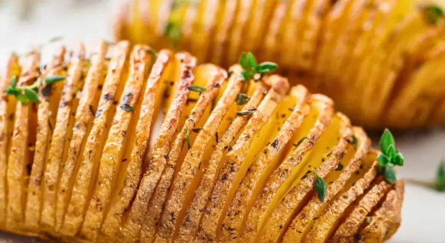 Deux pommes de terre hasselback dorées et croustillantes, garnies d'herbes fraîches. Un délice visuel et gustatif.
