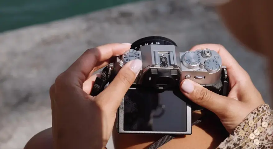 Dłonie trzymają srebrny aparat Fujifilm XT50, obracając pokrętło trybów filmowych.