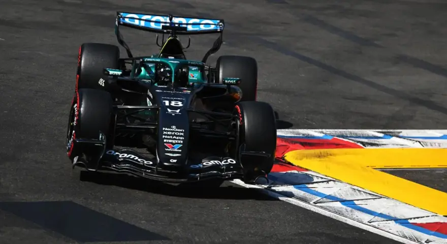 El coche de F1 Aston Martin número 18 se inclina en una curva, con sus neumáticos rozando la línea de la pista.