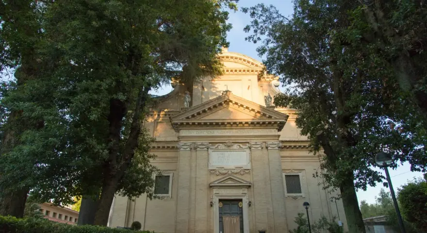 A serene church facade at Tre Fontane, Rome, bathed in golden light, framed by lush green trees.