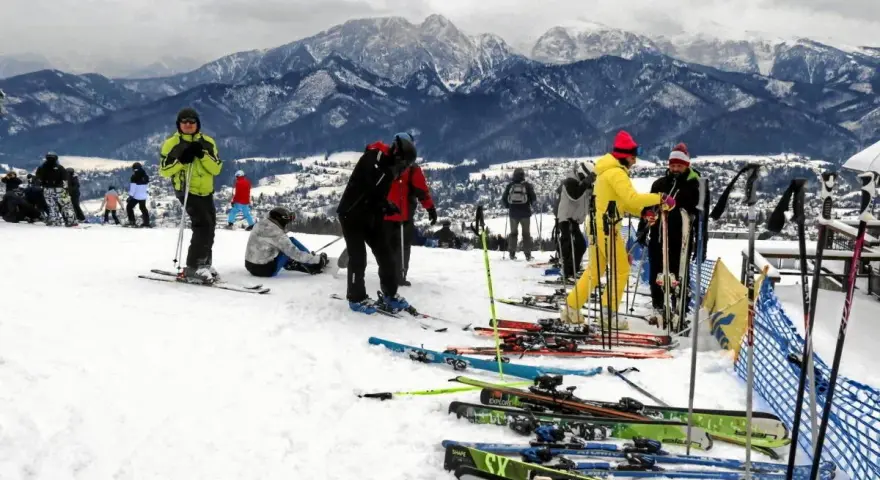 Ludzie na nartach i snowboardach na stoku, w tle góry. Zastanawiasz się, ile się idzie na Gubałówkę? Tu jest zimowo i aktywnie!