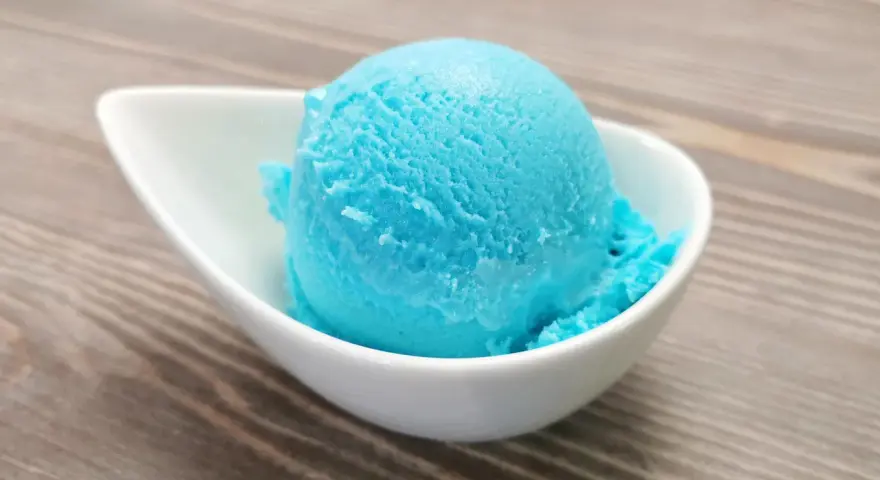 Ein Löffel leuchtend blaues Kaugummi Eis in einer weißen Schale. Perfekt für ein selbstgemachtes Kaugummi Eis Rezept.