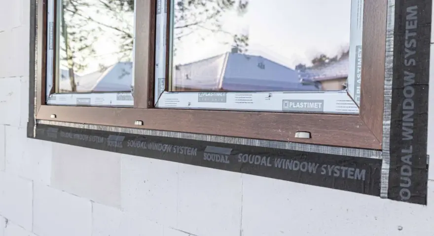 Ciepły montaż okien z użyciem taśmy Soudal Window System. Brązowa rama okienna na tle białego pustaka.