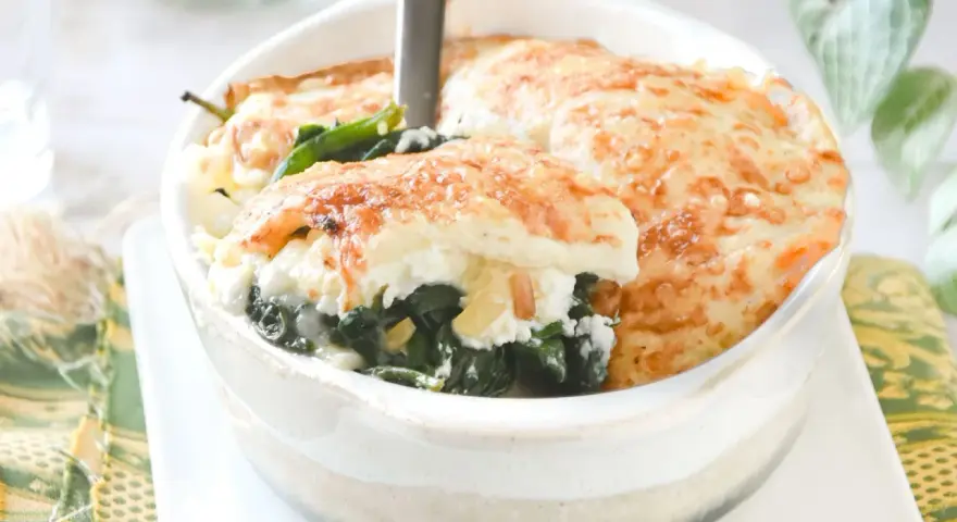 Deliciosa lasaña de espinacas gratinada, servida en un cuenco blanco. El queso dorado y burbujeante cubre las capas de espinacas y ricotta.