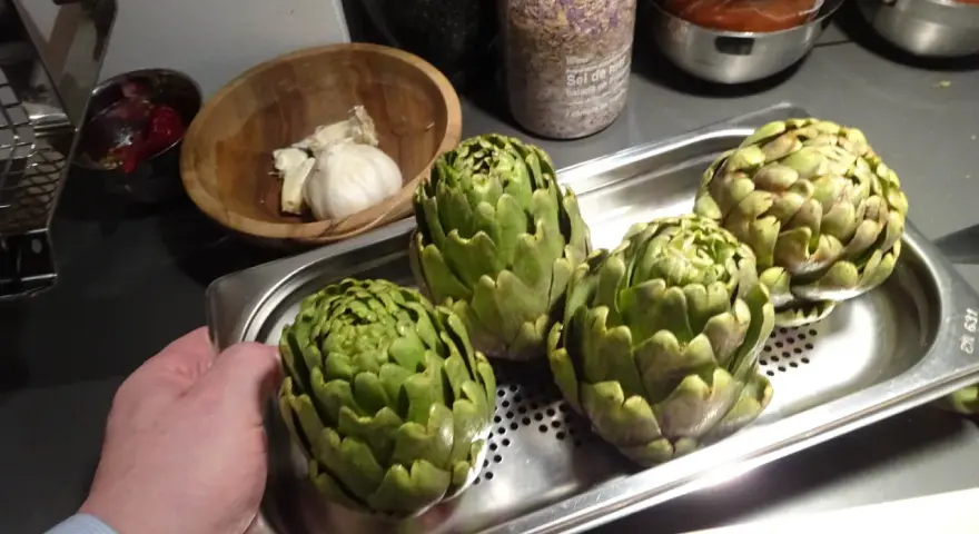 Quatre artichauts verts prêts pour la cuisson vapeur. Une main tient le plateau.