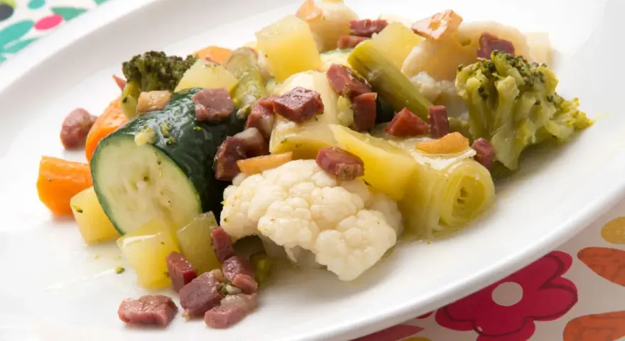 Un colorido panache de verduras con brócoli, coliflor, calabacín, zanahoria y patatas, salpicado de trocitos de jamón.