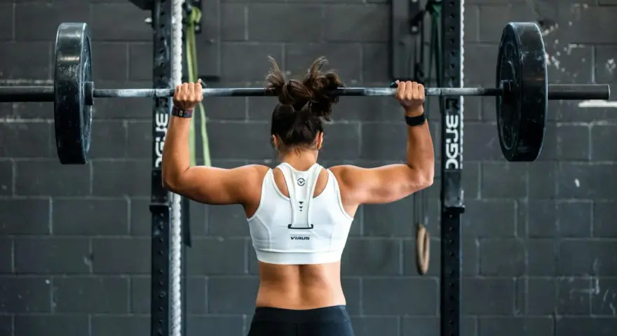 Femme musclée soulevant une barre chargée, prête pour un superset musculation intense.