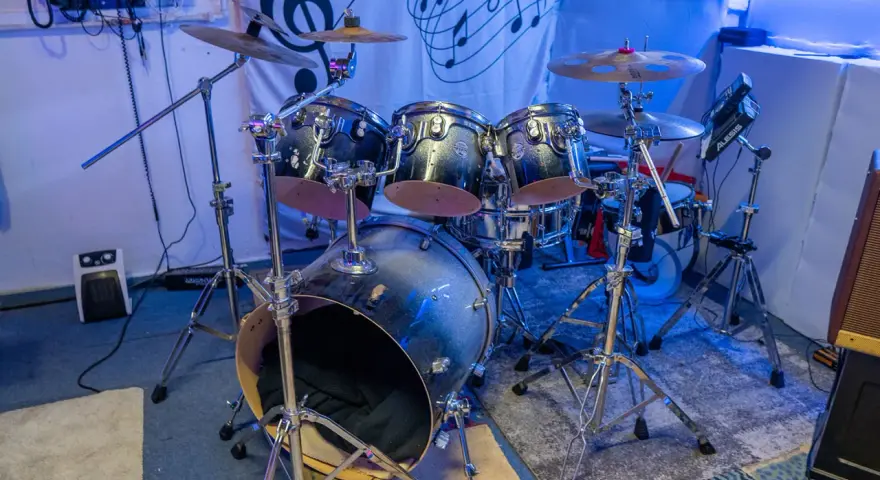Der **Aufbau Schlagzeug** ist bereit für den nächsten Gig. Glänzende Trommeln und Becken stehen auf stabilen Stativen, beleuchtet von blauem Licht.